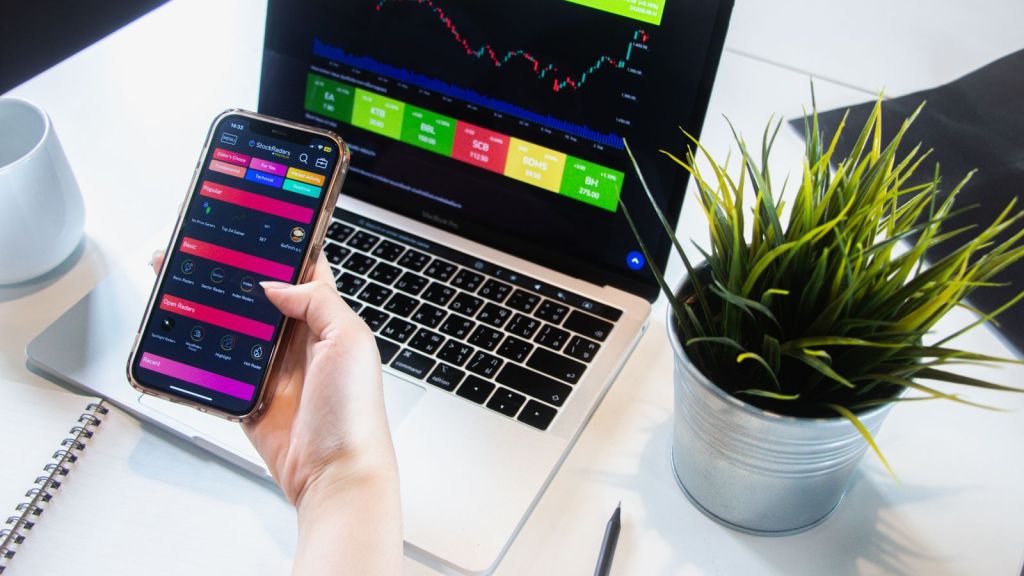 person trading stocks on phone and laptop